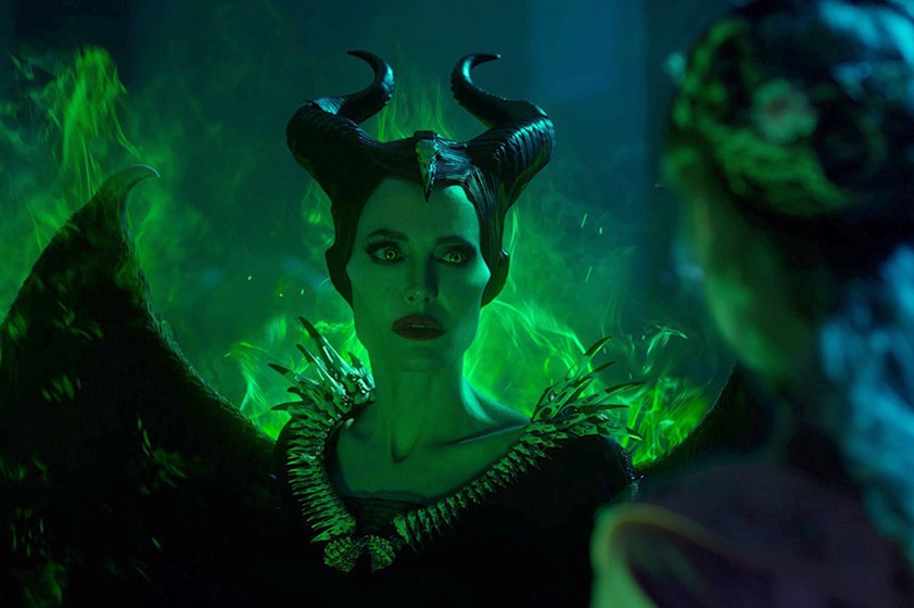 Angelina Jolie with black horns and wings is surrounded by bright green visual effects, and faces blonde figure with long hair.