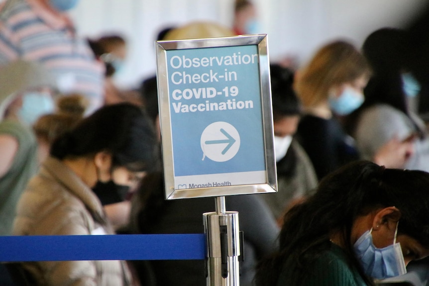 A sign about vaccination with a crowd of people in the background.