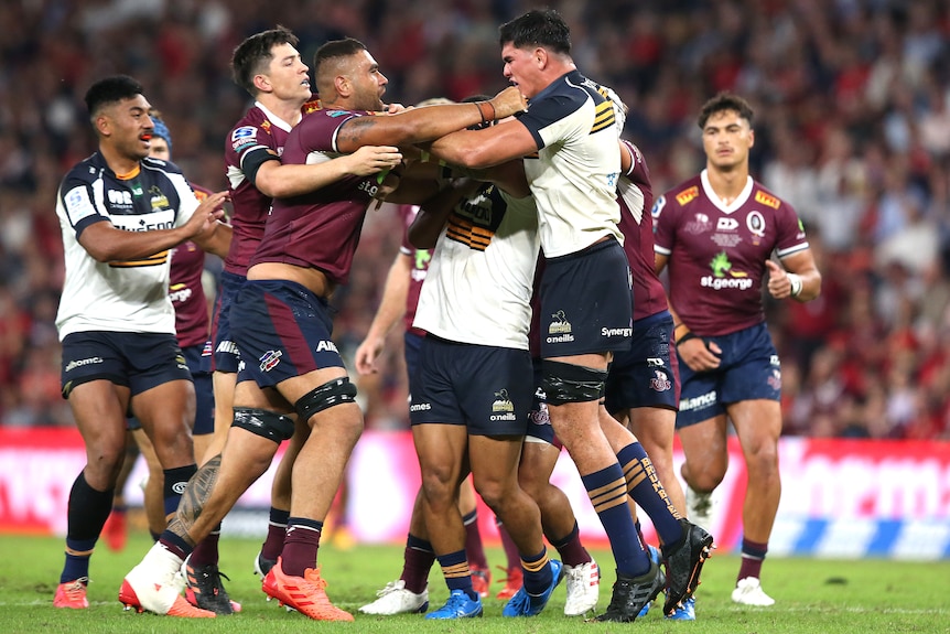 Rugby players wearing maroon and white fight each other during a game