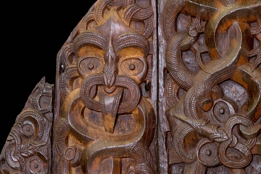Close up of an intricately carved wooden panel showing a deeply carved stylistic face.