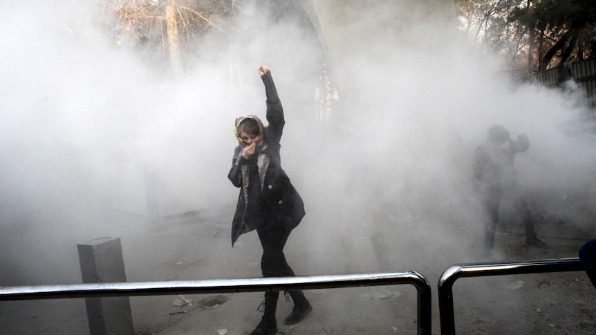 A woman stands with her arm raised in a cloud of smoke.