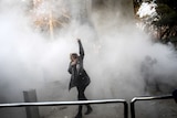 A woman stands with her arm raised in a cloud of smoke.