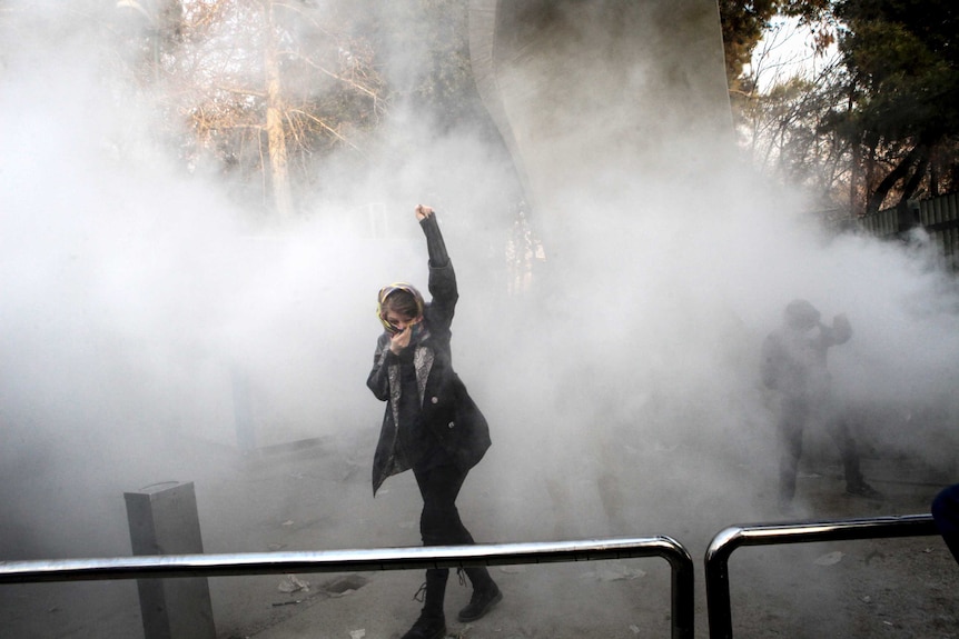 A woman stands with her arm raised in a cloud of smoke.