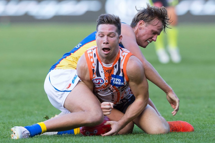 Toby Greene on his knees with his eyes closed as he is tackled by a Suns player.