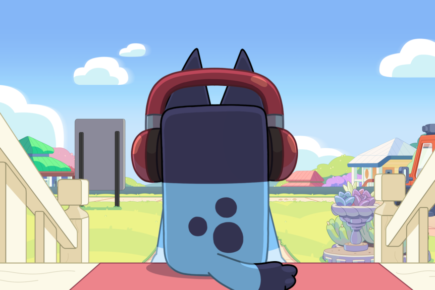 Bluey wearing headphones, sits on his front door step with her back to the camer.