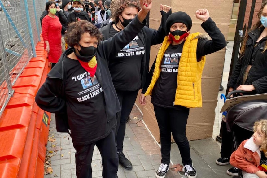 Three women wearing masks hold their fists in the air.