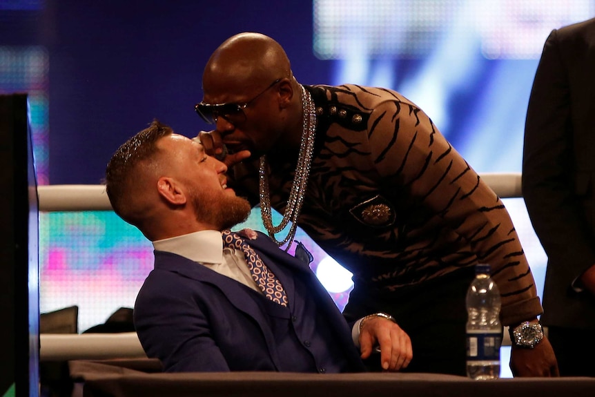 Floyd Mayweather screams in the face of Conor McGregor with a microphone.