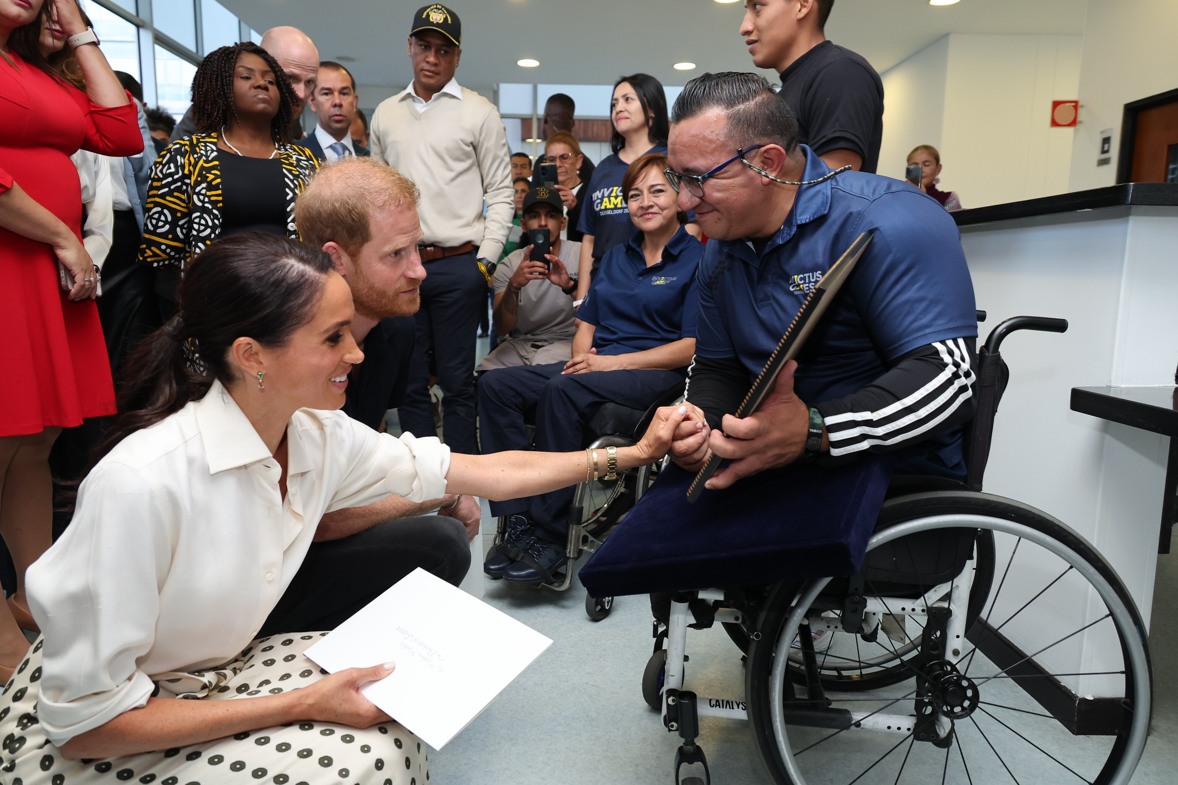Harry and Meghan crouch as they greet an athlete who is using a wheelchair.