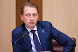 Liberal Senator James Paterson shown in a suit sitting at a desk during a Senate inquiry 