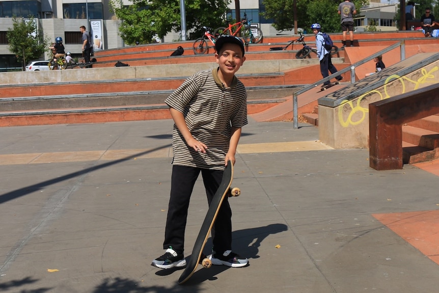 Boy wearing cap holding a skateboard. 