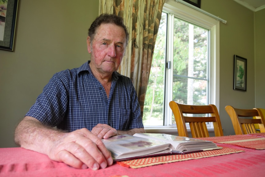 a man has a photo album out, looking at the camera, in his dining room