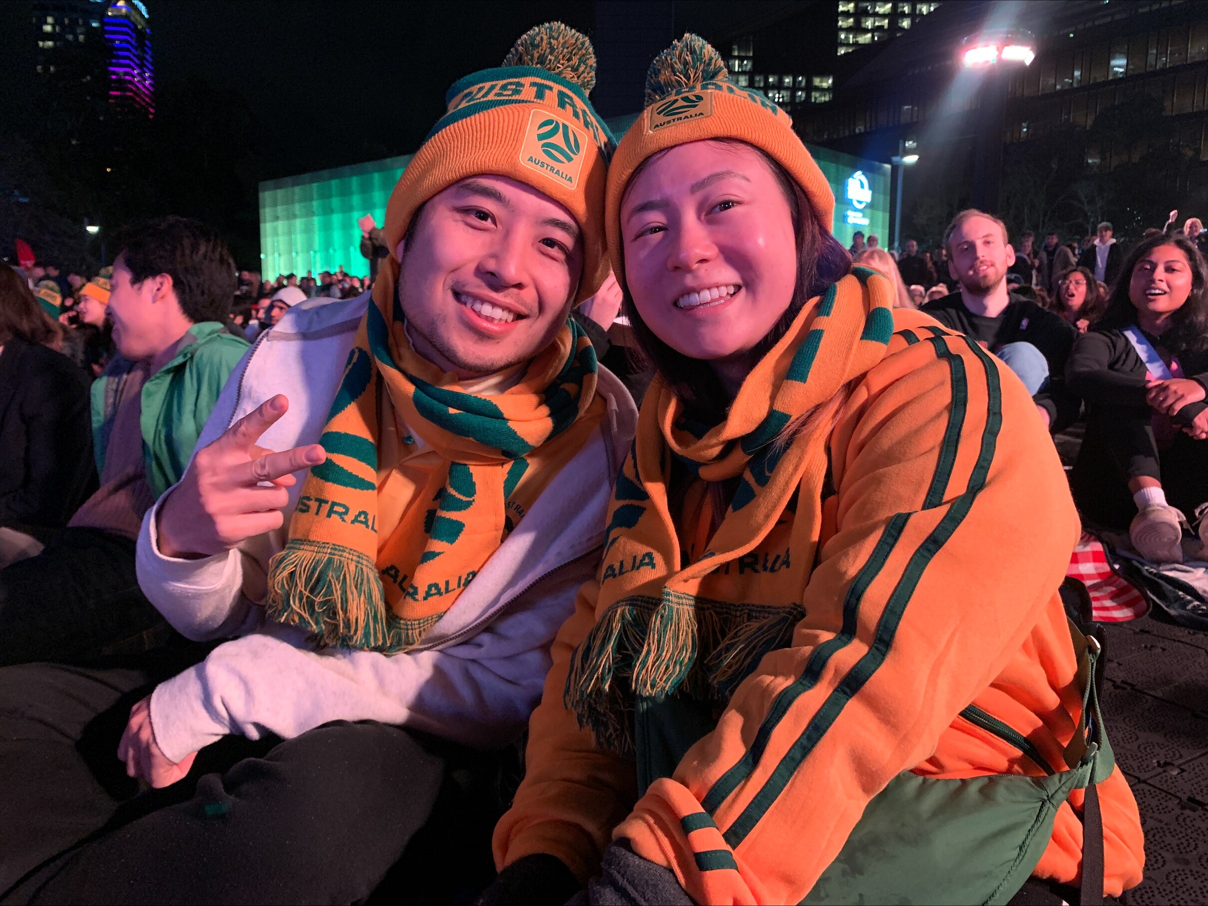 a couple smiling at the camera wearing australia scarves and beanies