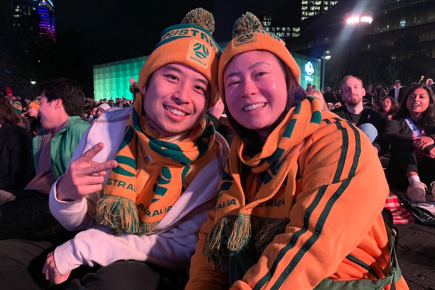a couple smiling at the camera wearing australia scarves and beanies