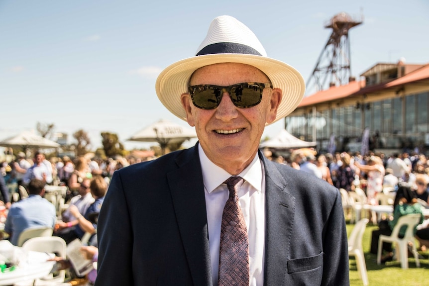 A man wearing a hat, sunglasses and suit and tie at the races.  
