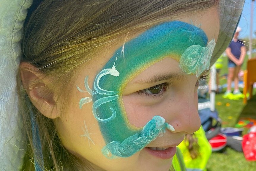 A young girl with green, blue and yellow face paint.