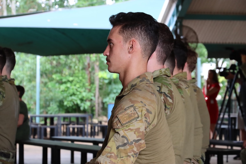 People wearing ADF uniform standing in a line under a cover, listening to a speech.