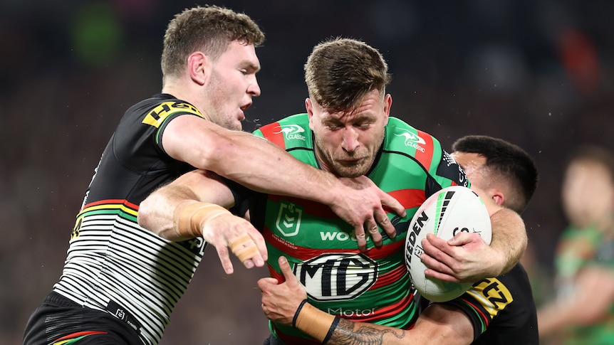 A South Sydney NRL player is tackled by two Penrith Panthers opponents.