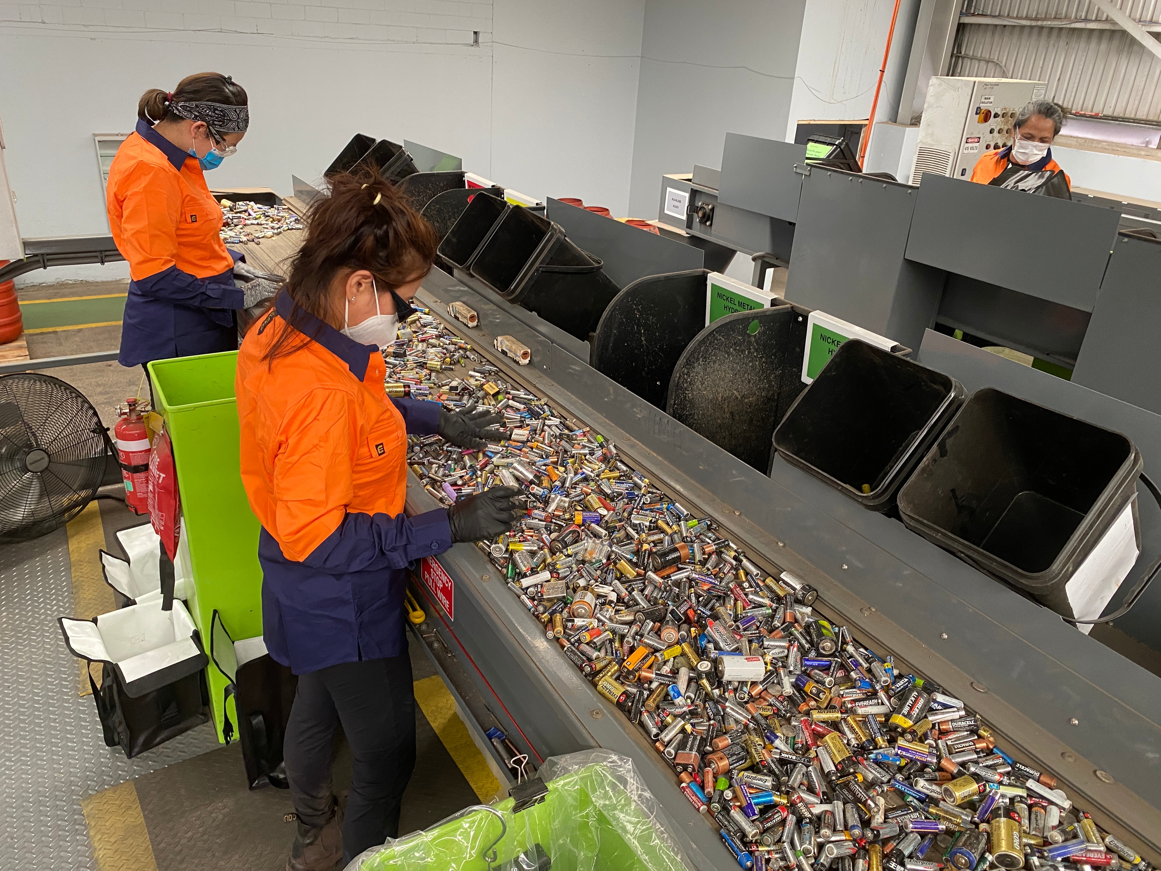 workers in high vis with a conveyer of small batteries