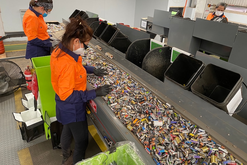 workers in high vis with a conveyer of small batteries