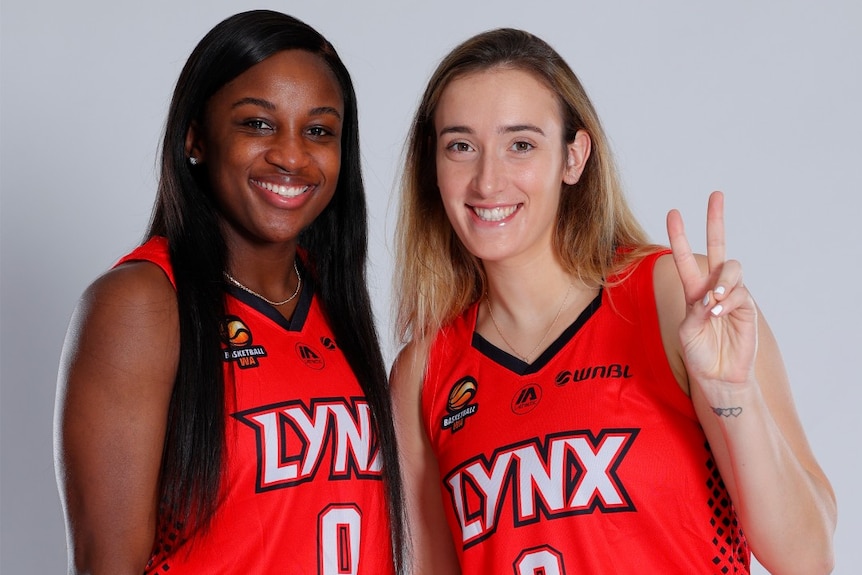 Two basketball players in Perth Lynx jerseys pose for a photo, one of whom holds up a peace sign.