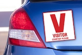 Digitally altered image depicting V-plate for visitors attached to rear of car.