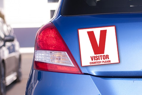 Digitally altered image depicting V-plate for visitors attached to rear of car.