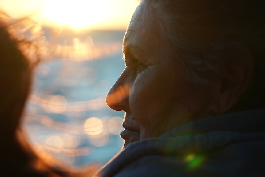 A 71-year-old woman looks out over the water at sunset. 