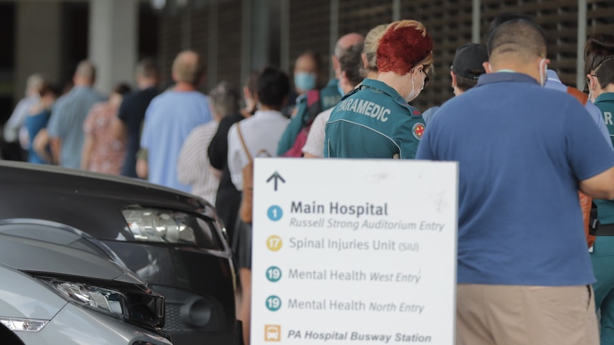 Una línea de personas con letrero que apunta al hospital principal. 