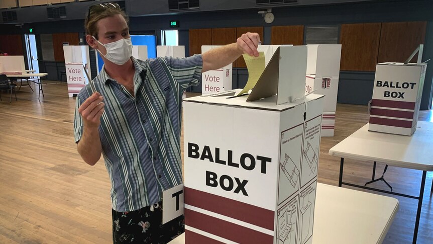 A man in a face mask placing his vote into a ballot box