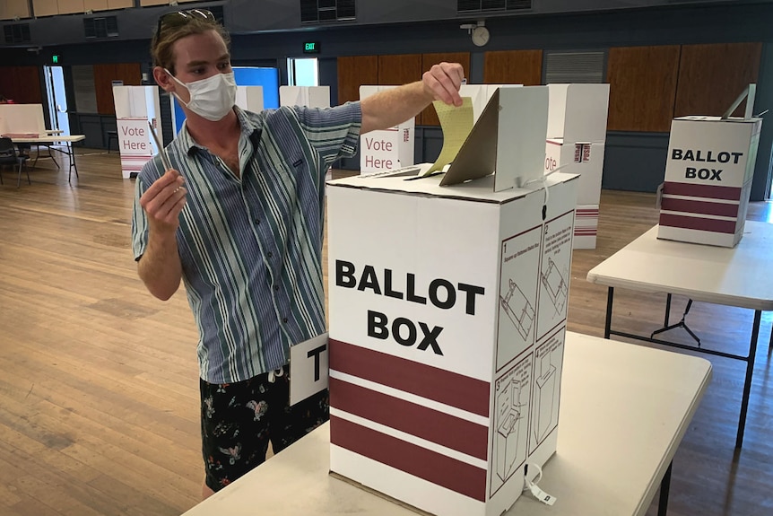A man in a face mask placing his vote into a ballot box