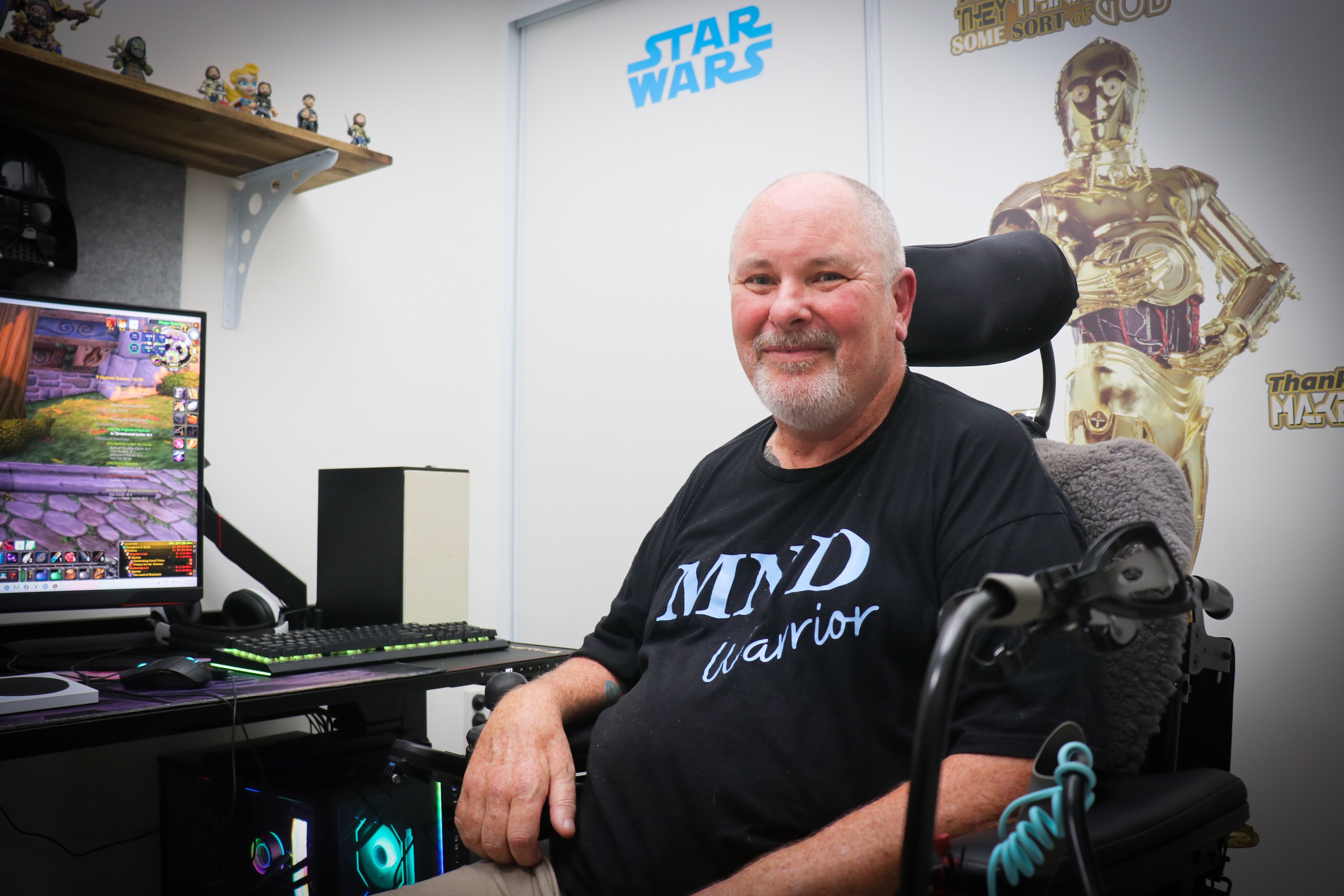 A man in a black Tshirt sitting in front of a computer game and smiling at the camera.