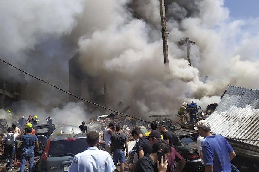 Smoke billows out above rescue workers, civilians and cars on suburban street 