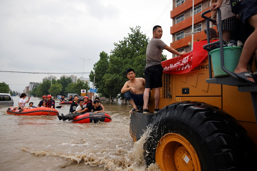 People riding boats and front loader make their way through a flooded road