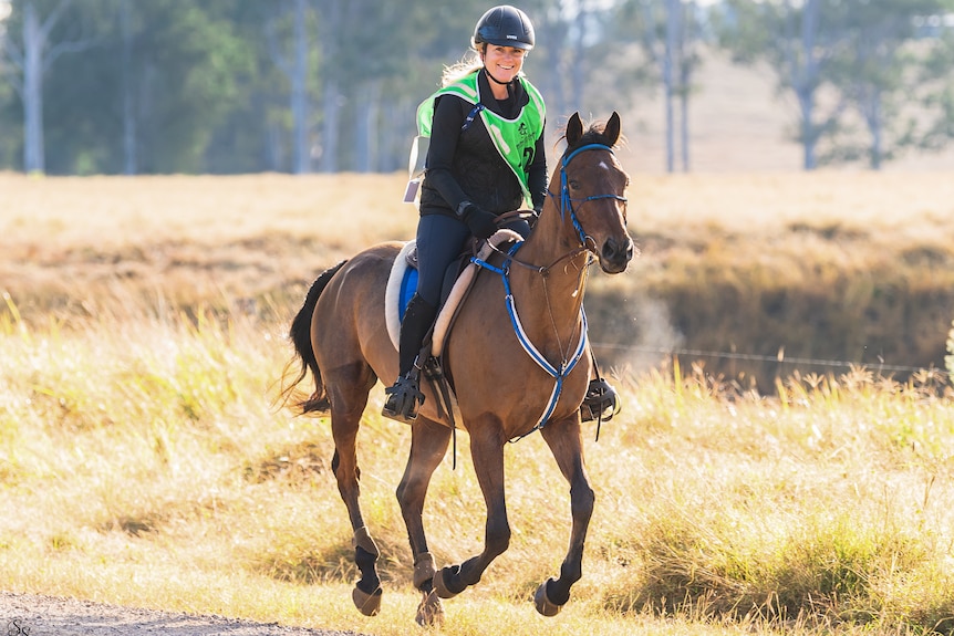 Women with a helmet on riding a horse.