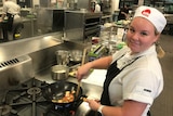 Ashley Groom cooks vegetables in a pan in her chef whites.