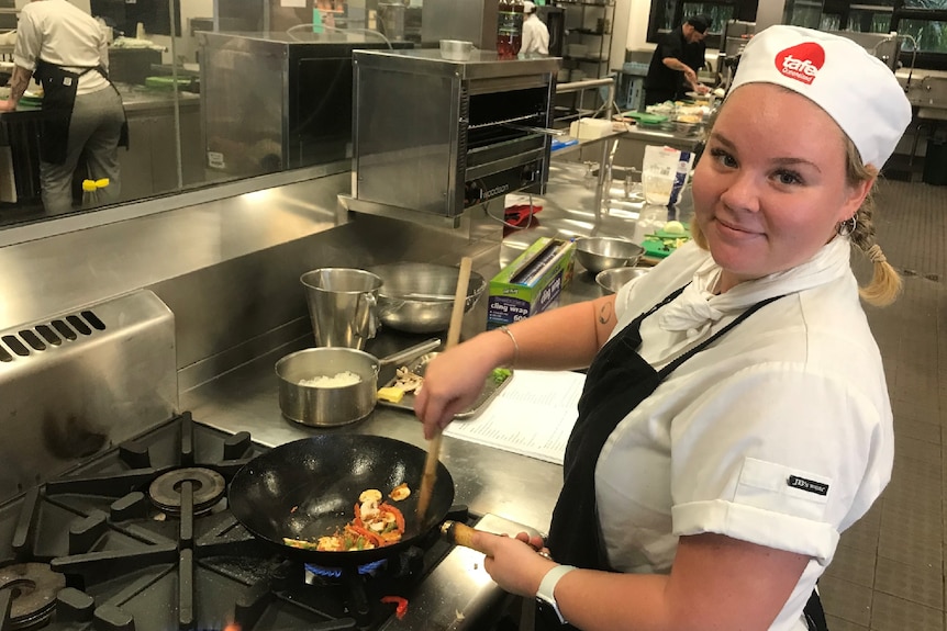 Ashley Groom cooks vegetables in a pan in her chef whites.