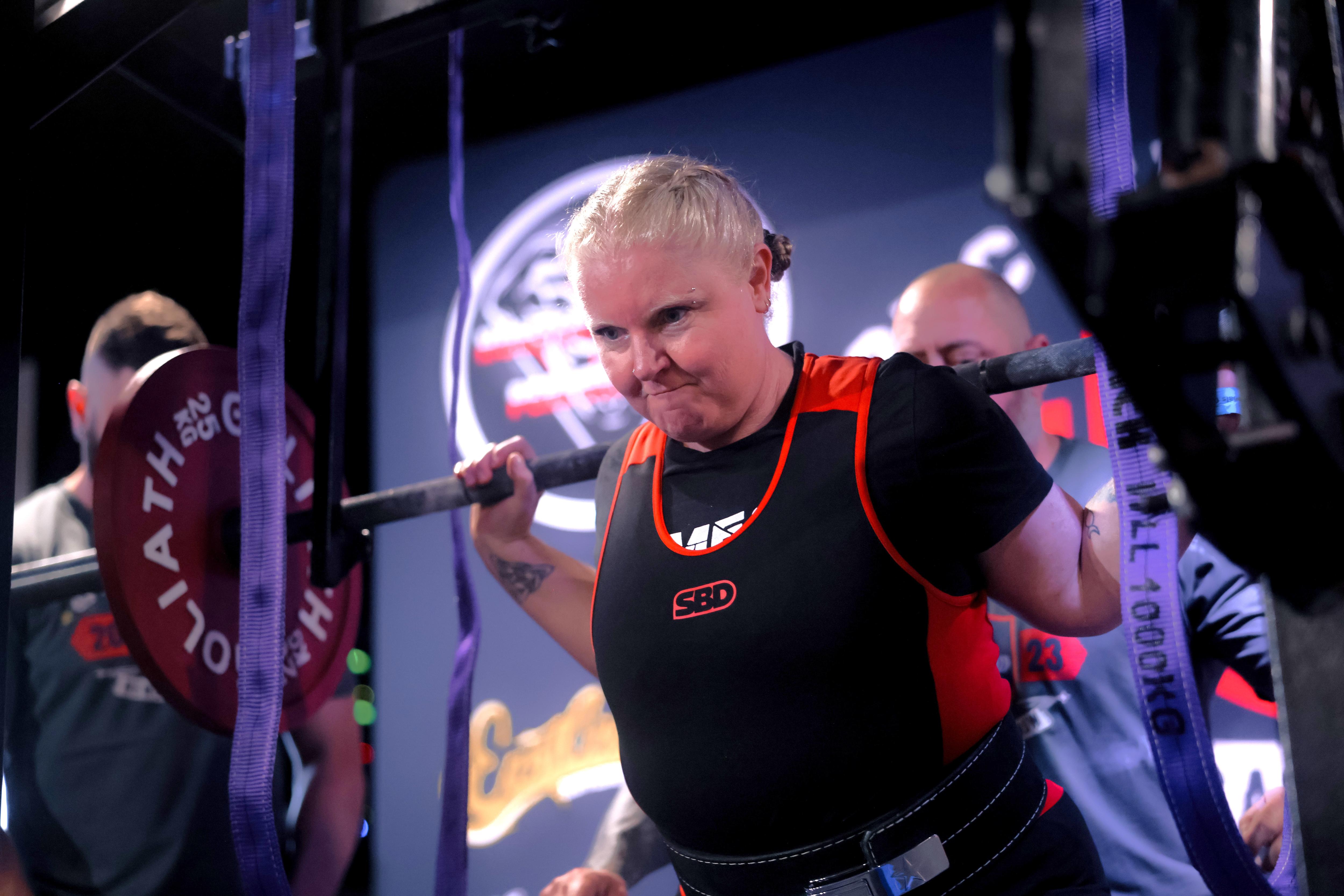a woman lifting weights while squatting with a serious expression on her face.