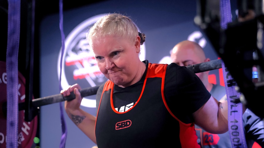 a woman lifting weights while squatting with a serious expression on her face.