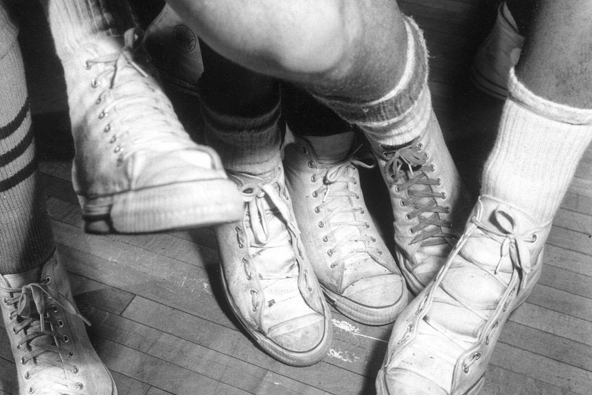 一张黑白照片中，一群人穿着球鞋的人们把脚放在一起。