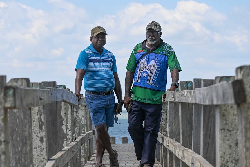 Two men stand on a boardwalk.