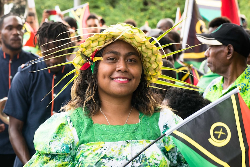 A woman holding a Vanuatu flag smiles for a photo.