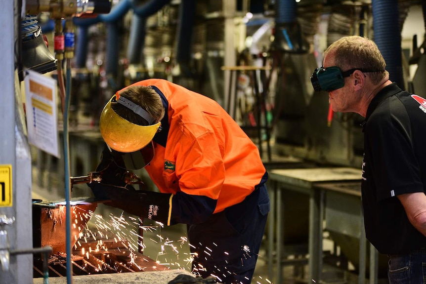 Nathanial Bradford welding wearing safety gear at his workplace as his TAFE teacher Ronald Dyer looks on wearing safety glasses.