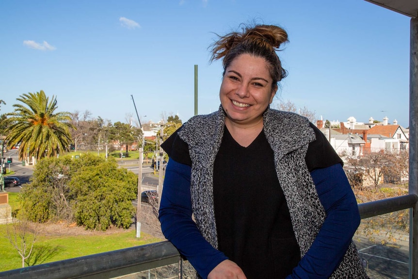 A woman stands on a balcony in inner city Melbourne.