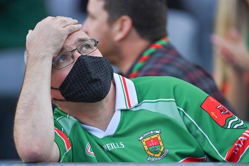 A mask-wearing fan in Mayo colours puts his hand over his forehead amid the stress of an All-Ireland football final. 