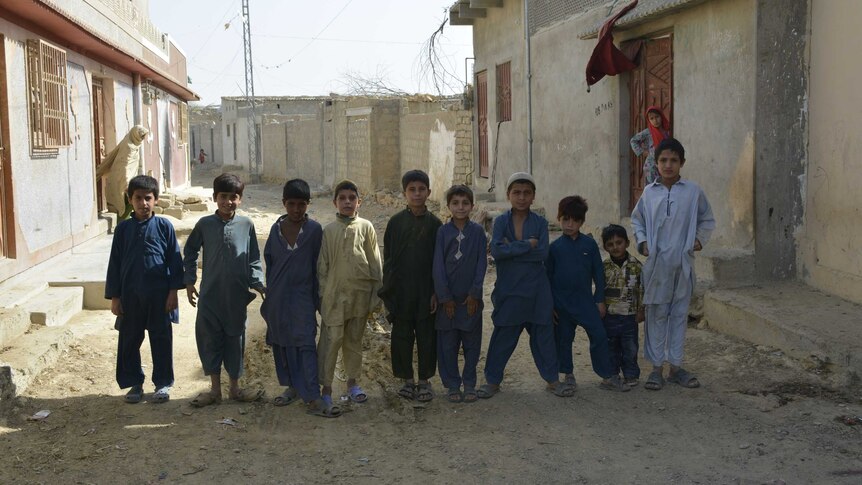 Ten young boys stand in a row on a run-down street in Pakistan.