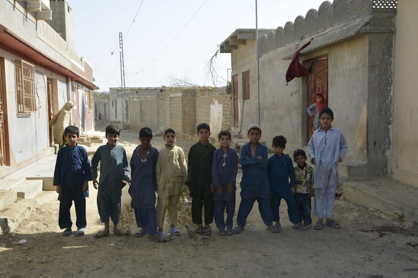 Ten young boys stand in a row on a run-down street in Pakistan.