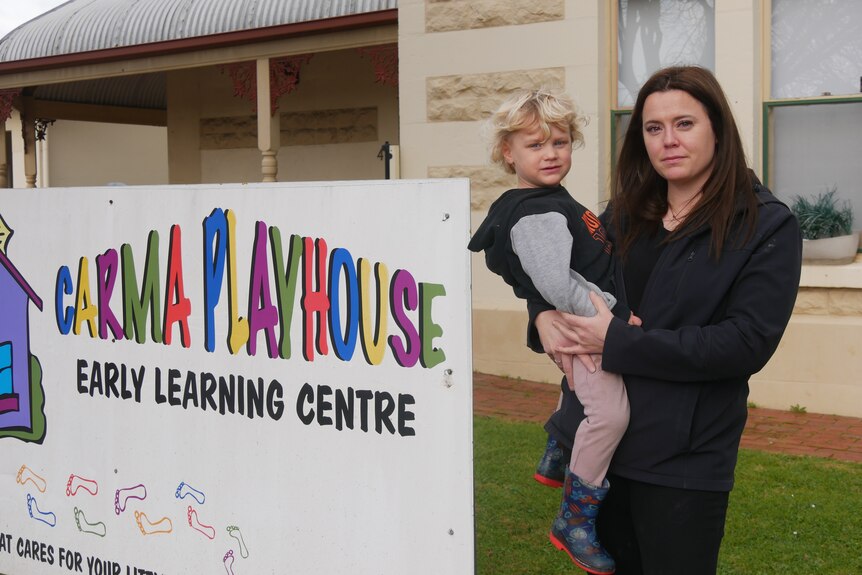A woman holds a young boy in front of a childcare centre