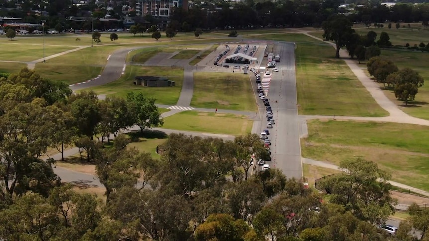 A drone photo of cars lined up to and around a tent in a park
