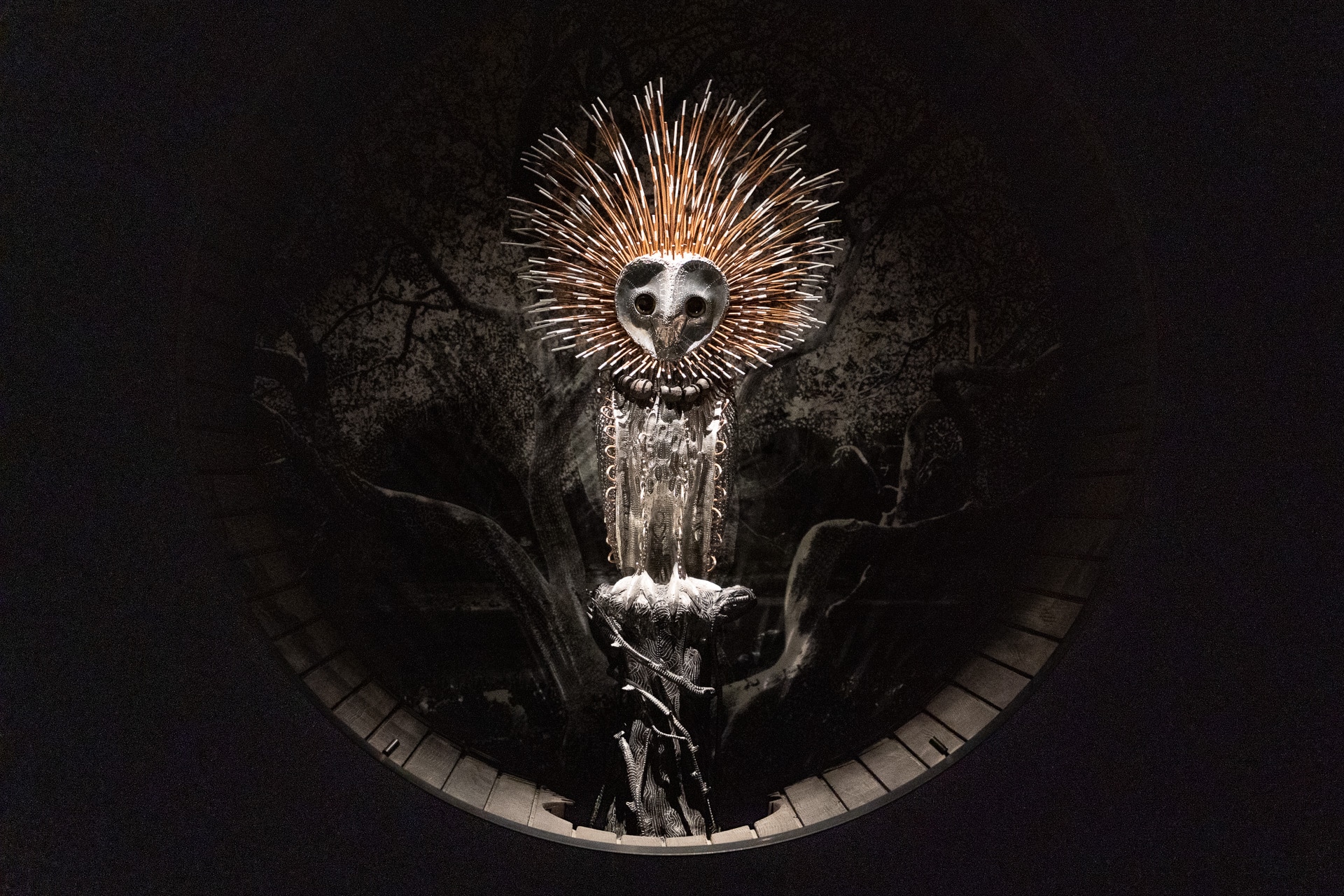 An artwork showing a lit-up owl, perched in a tree. It is surrounded by darkness.