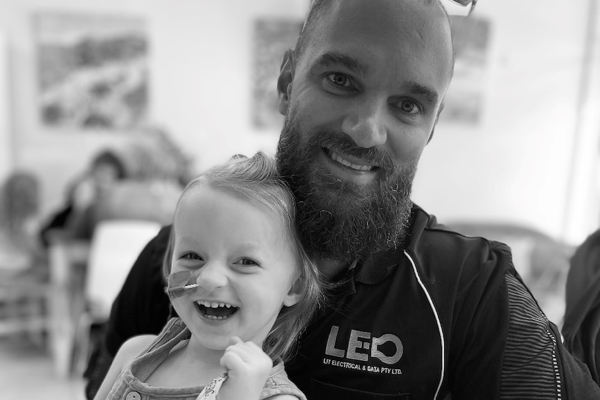 A black and white image of a little girl with a feeding tube and her dad